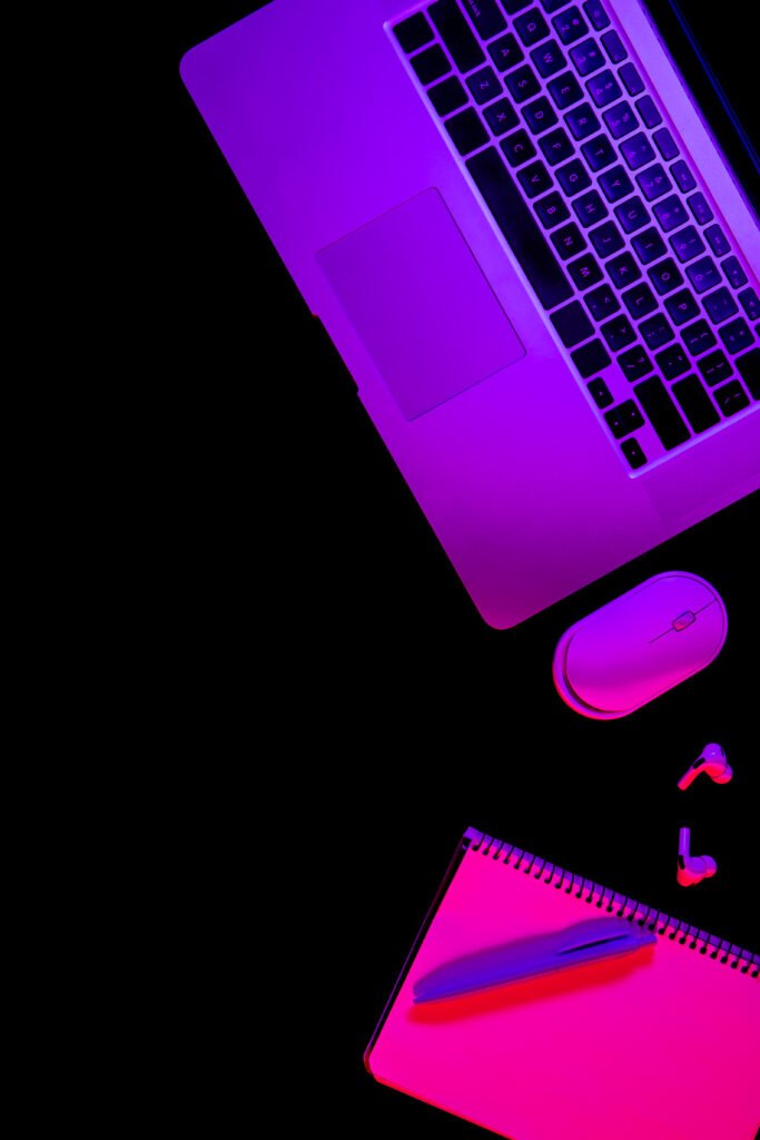 laptop and notepad on black background with neon light, flat lay.